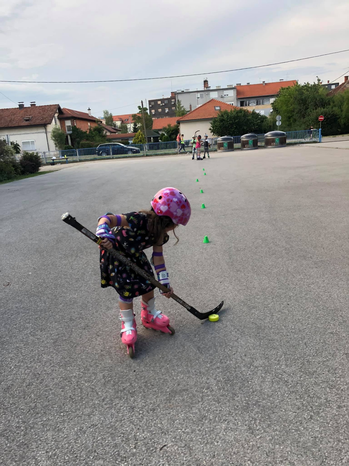 Mala djevojčica na rolama vodi pak hokejaškom palicom pored niza zelenih čunjeva